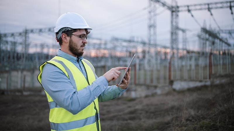 A person in a safety vest and hardhat holding a tablet