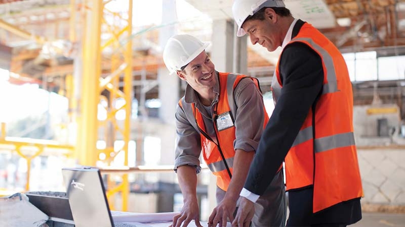 A few men wearing safety vests and helmets looking at a computer